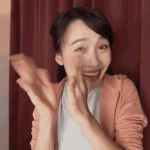 a woman in a pink jacket is smiling and clapping her hands .