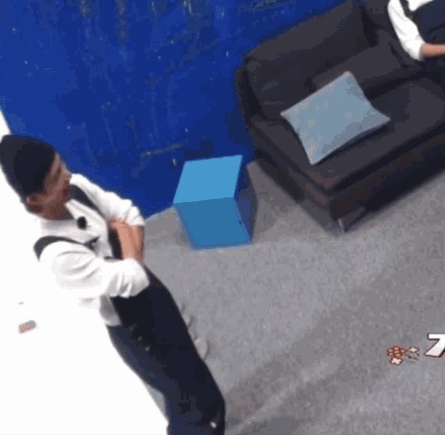 a man in a black hat stands in a room with a couch and a blue box