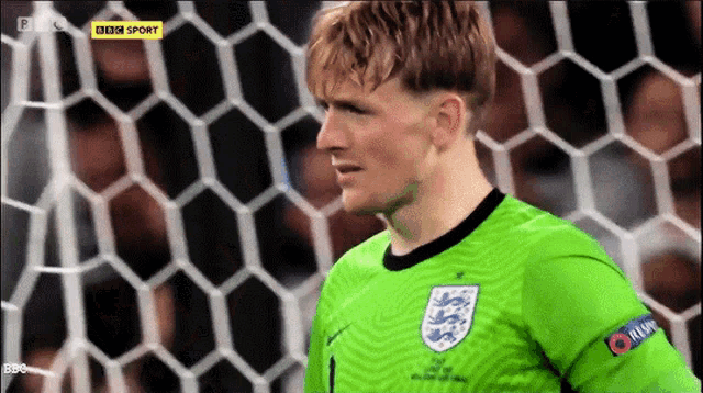 a soccer player in a green jersey stands in front of a bbc sport logo