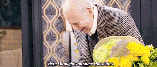 a man in a suit is holding a bouquet of yellow flowers and says `` here i brought you some chocolates '' .
