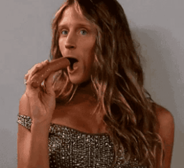 a woman in a strapless dress is eating a chocolate bar