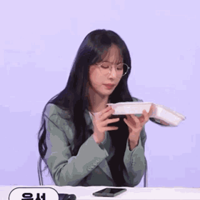 a woman is sitting at a table holding a box in her hands .