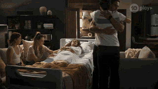 a group of people standing around a woman in a hospital bed that is sponsored by play