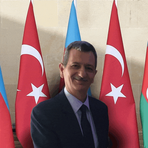 a man in a suit and tie stands in front of flags
