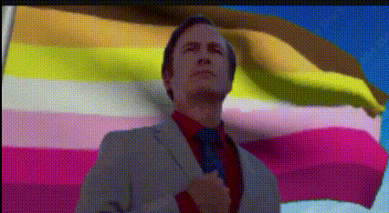 a man in a suit and tie stands in front of a rainbow flag