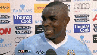 a man in a blue shirt is talking into a microphone in front of advertisements for barclays thomas cook and audi