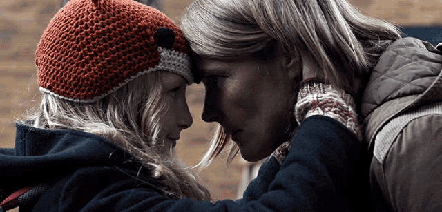 a woman wearing a knitted hat is hugging a young girl