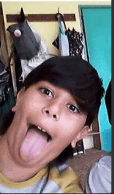 a young boy is sticking his tongue out while taking a selfie in a room .