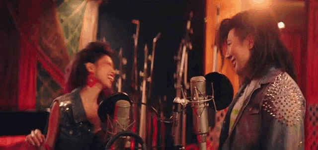 two women are singing into microphones in a studio .