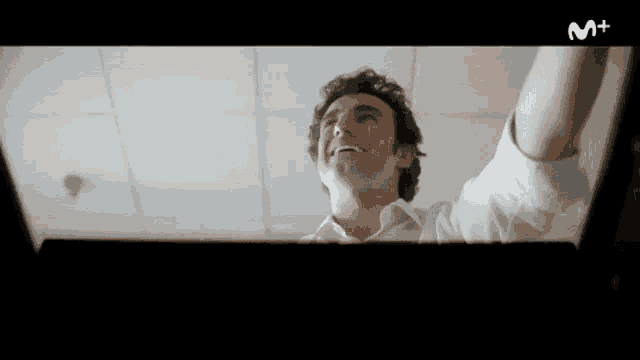 a man in a white shirt is smiling while looking up at the letter m above him