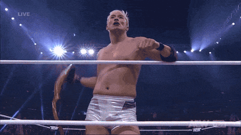 a shirtless wrestler is standing in front of a screen that says live