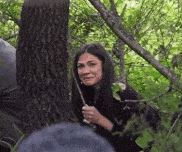 a woman is peeking out from behind a tree in a forest .