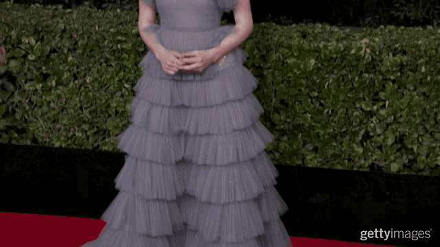 a woman wearing a gray ruffled dress is standing on a red carpet