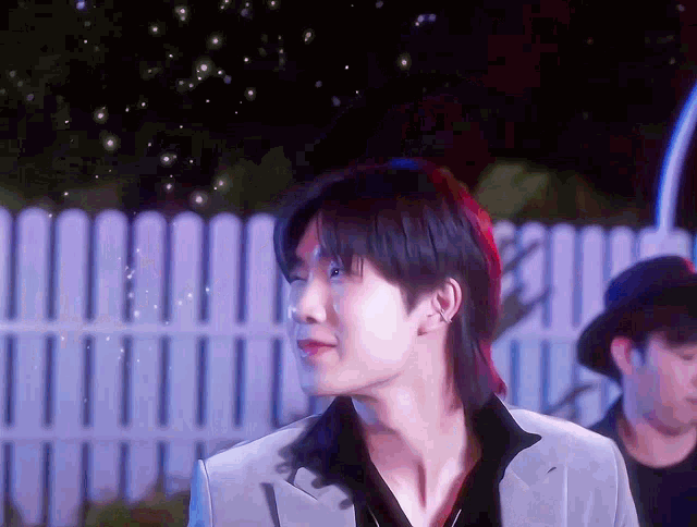 a man with a mullet is standing in front of a white fence