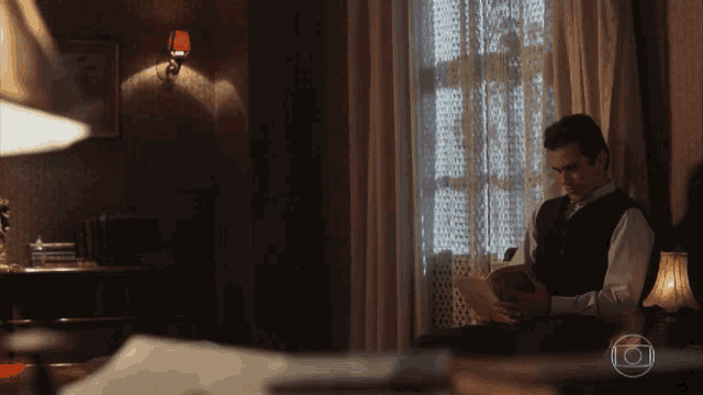 a man is reading a book in a dark room with a lamp