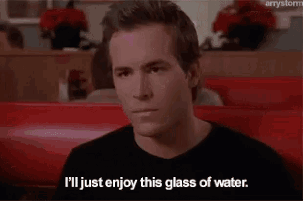 a man in a black shirt is sitting in a diner and saying i 'll just enjoy this glass of water