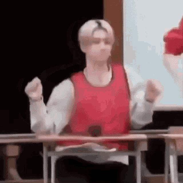 a man in a red vest is sitting at a desk .