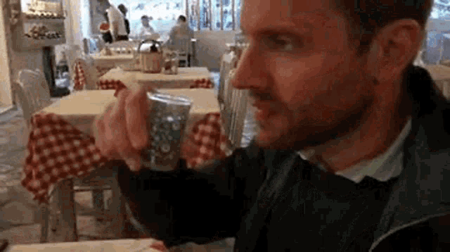 a man is sitting at a table in a restaurant holding a cup of coffee .
