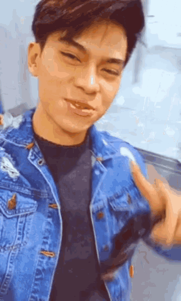 a young man wearing a denim jacket is taking a picture of himself