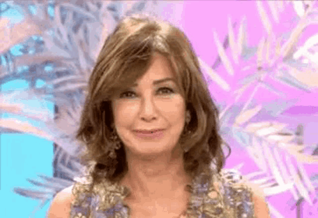 a woman in a purple dress is smiling in front of a pink background with palm leaves .