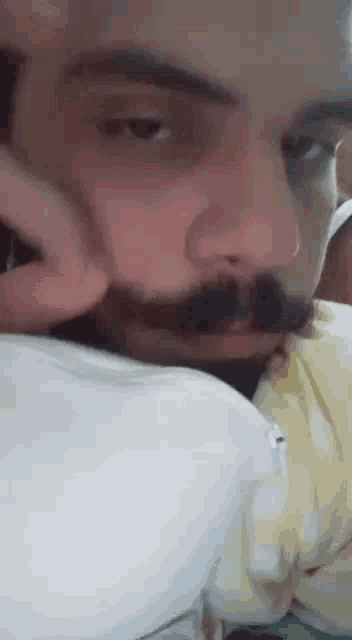 a man with a beard and mustache is laying on a bed with his hand on his face .