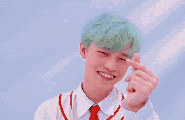 a young boy with green hair is making a heart with his hands