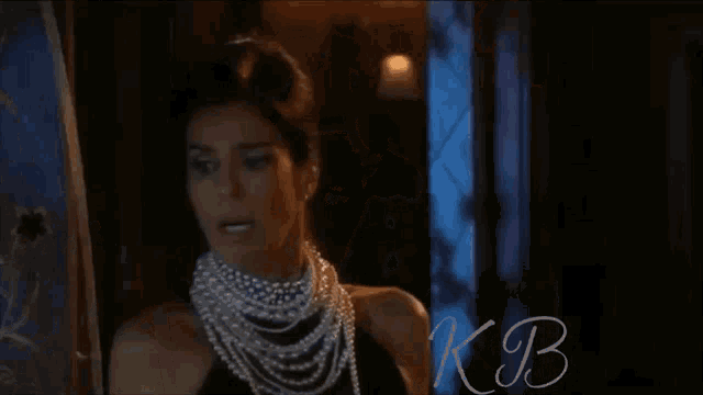 a woman wearing a pearl necklace and white gloves has kb written in blue
