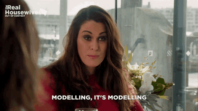 a woman is sitting at a table with flowers and says modelling