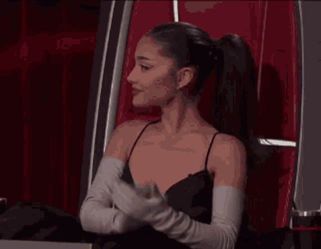 a woman in a black dress and white gloves is sitting in a red chair .