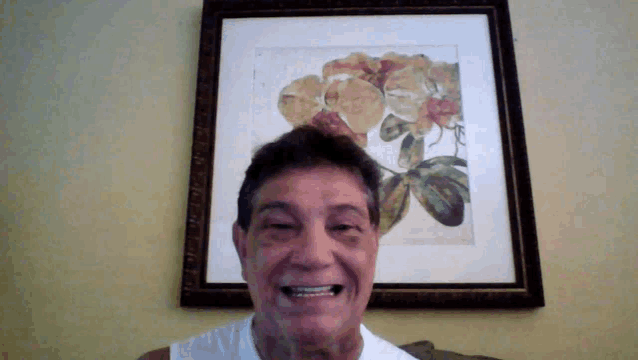 a man smiles in front of a framed painting of flowers