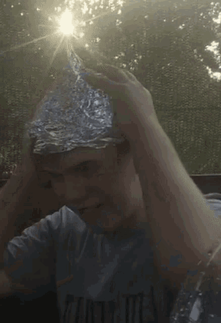 a man wearing a tin foil hat with the sun shining through the trees