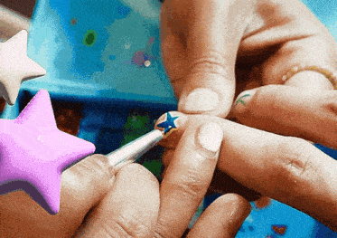 a person is painting their nails with a pink star and a blue star