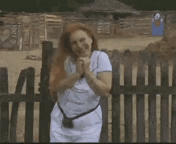 a woman with red hair is standing next to a wooden fence