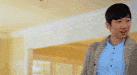a young man wearing a blue shirt and a gray sweater is standing in a hallway .