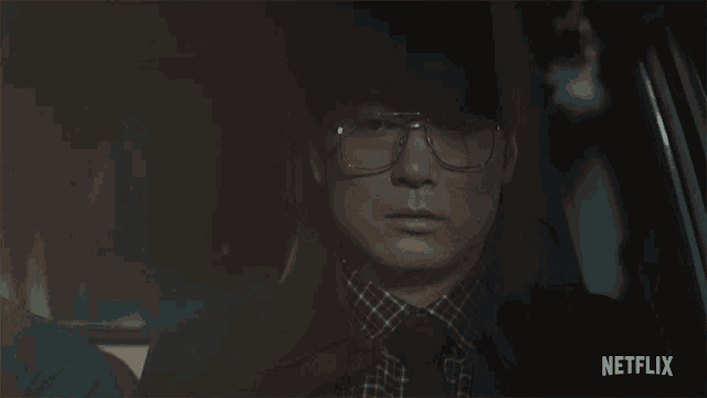 a man wearing glasses sits in a car with netflix written on the bottom