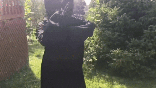 a person in a black hooded jacket is standing in the grass with their arms crossed