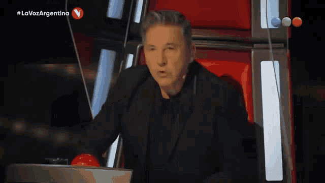 a man in a black suit is sitting in front of a red button that says lavoz argentina