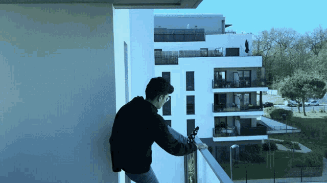 a man is standing on a balcony looking out at a building