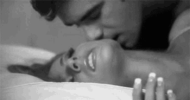 a black and white photo of a man kissing a woman on the neck .