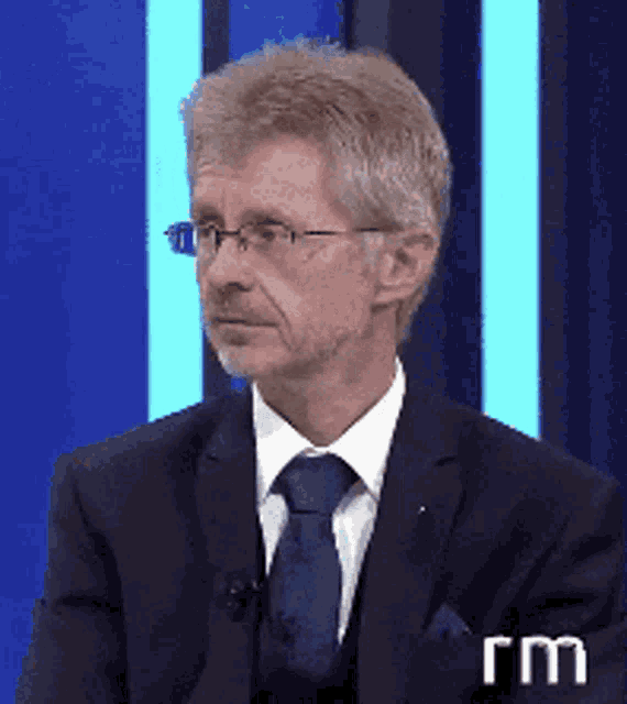 a man in a suit and tie is sitting in front of a blue background with the letters rm on it