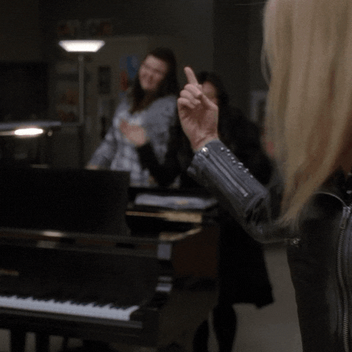 a woman in a black jacket stands in front of a black piano