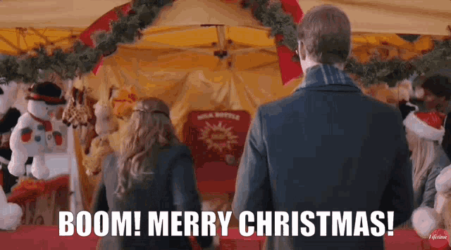 a man and a woman are standing in front of a tent with the words boom merry christmas written on it