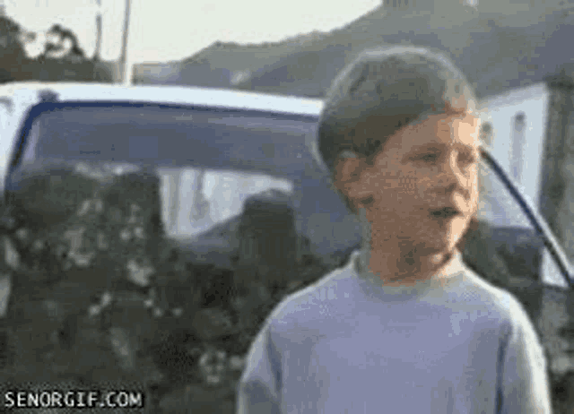 a young boy is standing in front of a car and making a face .