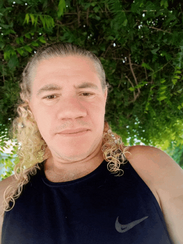 a man with a ponytail wears a blue nike tank top