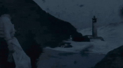 a person is standing in front of a lighthouse in the middle of the ocean at night .
