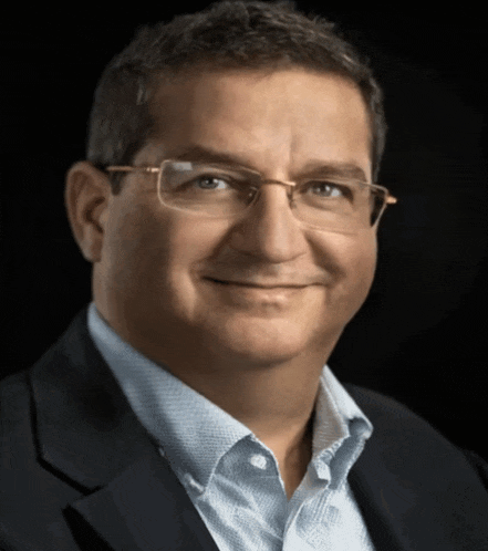 a man wearing glasses and a suit looks at the camera