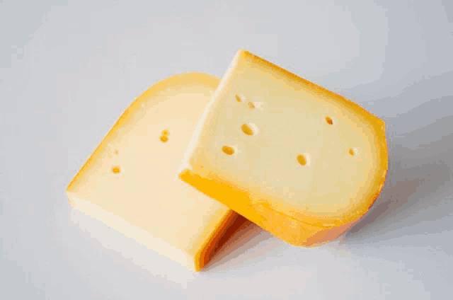 two slices of yellow cheese with holes in them on a white surface
