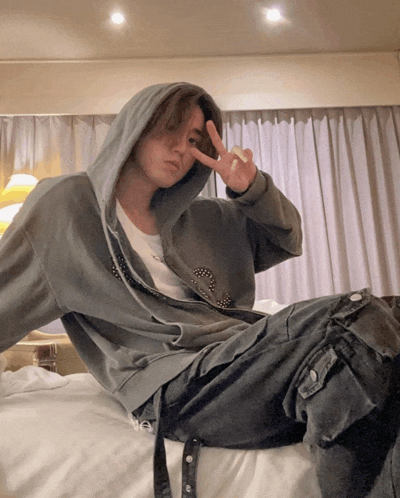 a person wearing a hoodie and jeans giving a peace sign