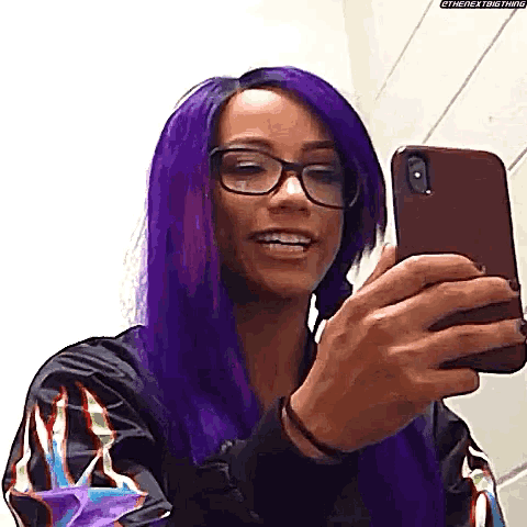 a woman with purple hair and glasses is taking a selfie on her cell phone .