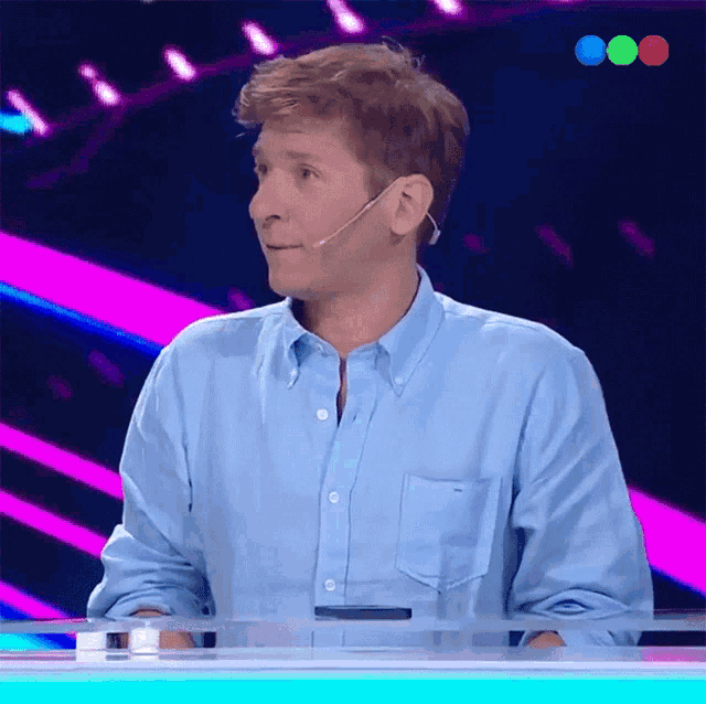 a man wearing a blue shirt and a microphone stands in front of a colorful background